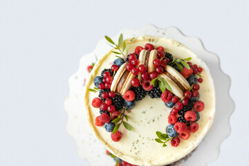 Top view of light coloured birthday cake decorated with fresh berries and macaroons cake. Beautiful dessert on white background