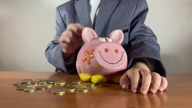 Kids savings. Preschool boy in a business suit putting coins in the piggy bank. Clos eup no face. High quality 4k footage