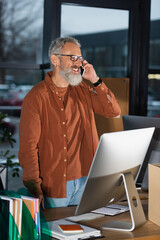 Grey haired businessman in casual clothes talking on cellphone near papers and commuter in office