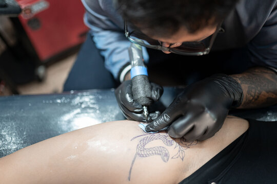 A tattoo artist is tattooing a snake on a woman's leg
