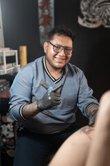 Portrait of a brunette tattoo artist posing smiling with his tattoo machine while working