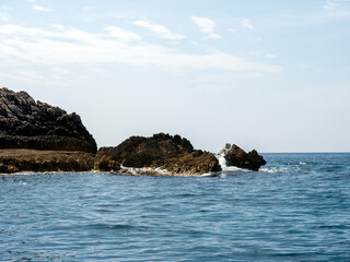 Fototapeta na wymiar Massive rock pices in sea with white wave foam under clear blue sky