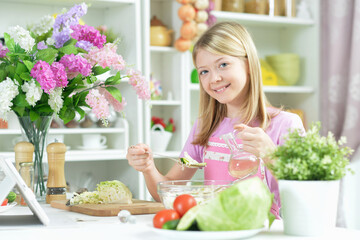 girl preparing fresh salad on kitchen table with tablet at home