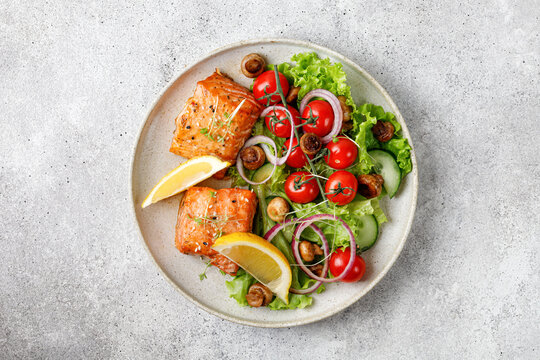 Salmon with green fresh vegetable salad, tomatoes cherry, onion on ceramic plate. Concept keto diet healthy food. Dinner idea.