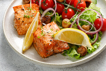 Fried Salmon steak fillet with fresh green salad with vegetables, tomatoes, onion, lemon in a plate. Keto diet concept healthy food, close up.