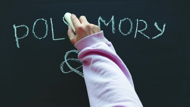 Close-up of a timelapse of a child's hand writing with chalk on a board - polyamory. The concept of love, openness, sex education, relationship, diversity and acceptance