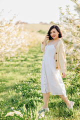 an attractive brunette in a white dress in a blooming spring garden. solar glare