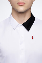 Cropped close-up shot of a young man in a black and white shirt decorated with a lapel pin in a red cross form. A cross lapel pin is on a shirt on a white background. Front view.