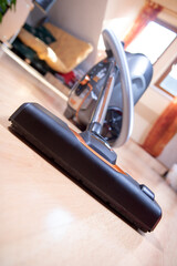 The Vacuum Cleaner on a laminate floor at room with windows on background. Cleaning the wooden floors with hoover, close up view.