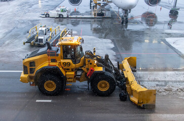 A bulldozer shovels snow from a snowy runway