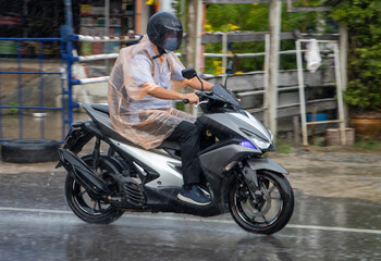 Fototapeta na wymiar A man in a raincoat rides a motorcycle on the street in heavy rain