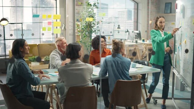 Collaborative Multiethnic Team Group Attending a Meeting to Develop a Strategy. Young Female Manager Using a Whiteboard to Explain Plan Steps. Colleagues Following her Presentation