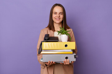 Horizontal shot of smiling friendly woman wearing beige jacket holding lot of documents folders...