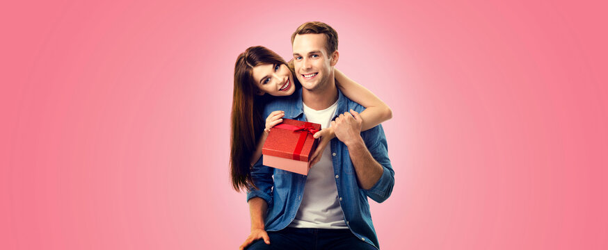 Holiday sales actions, rebates, discounts offers concept image - happy smiling couple opening gift box, isolated on vivid rose pink background. Copy space for some text.