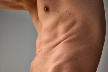 Fototapeta na wymiar Cropped image of male body, belly over grey studio background. Body positivity. Low fat level. Sportive body. Men's health and beauty