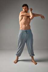 Stretching hands. Mature muscular man with relief body posing shirtless, in pants over grey studio background. Men's health and beauty