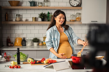 Beautiful pregnant woman filming cooking vlog. Happy woman filming her blog about healthy food at home..