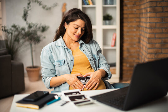 Beautiful young pregnant woman looking at ultrasound pictures of her baby. Businesswoman in office..