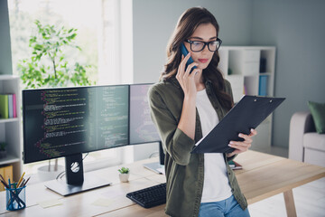 Photo of serious confident lady administrator wear spectacles talking modern device looking list...