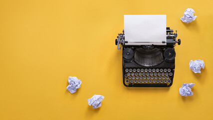 Vintage typewriter and crumpled papers over yellow background with copy space - obrazy, fototapety, plakaty