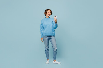 Full body young smiling happy woman wear knitted sweater look camera hold in hand use mobile cell...
