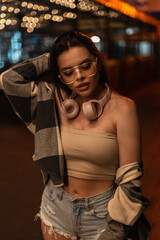 Fashionable beautiful stylish hipster model girl with glasses and pink headphones in a fashion top...