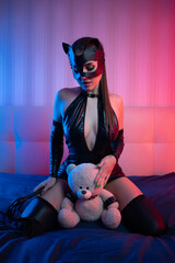 Sexy girl in latex dress bdsm in a cat mask on a bed in neon light