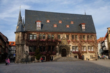 Obraz premium Quedlinburg, Saxony-Anhalt, Germany, 28 October 2022: Historic gothic townhall or Rathaus with Roland statue in Market Square, vintage colored timber frame houses in medieval town at sunny autumn day