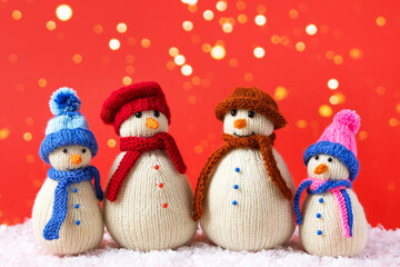 Family of knitted snowmen celebrate the holidays on a red background with golden lights. Winter fairy tale story with your own hands, hobby. Merry Christmas and New Year 2023 greeting card