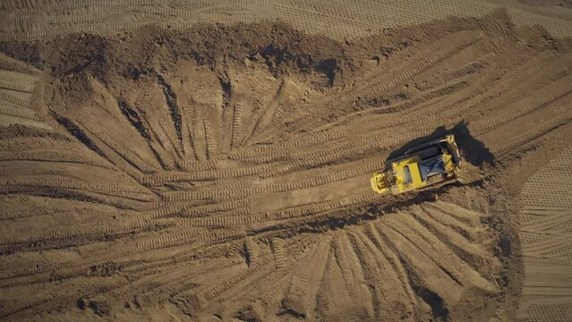 Yellow tracked Bulldozer drops the ground with a bucket - aerial top view shot. Earth construction works. Construction of the road with a bulldozer.