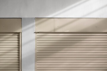 Light and shadow on part of 2 beige steel roller shutter doors of warehouse, front view with copy space