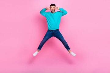 Fototapeta na wymiar Full length photo of young handsome male jumping showing v-sign spread legs wear trendy blue outfit isolated on pink color background