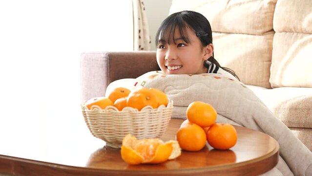 テレビを見ながらこたつでみかんを食べているアジア人の女性
