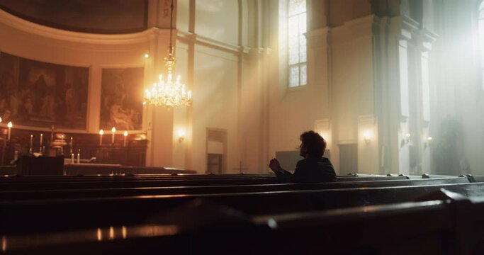 Young Christian Man Sits Piously in Majestic Church, with Folded Hands He Seeks Guidance From Their Religious Faith and Spirituality while Praying. Christianity and Belief in Power and Love of God