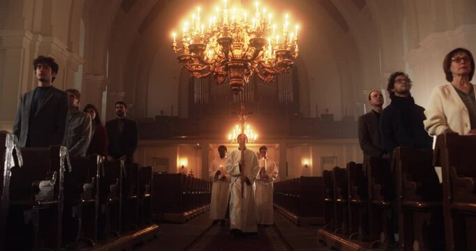 Beginning of a Liturgy In Grand Church where Priests, Deacons, Pastors Holding Processional Cross Walk in Ceremonial Procession. Beginning of the Mass Service with Devout Parishioners Standing