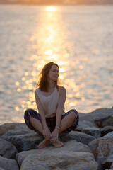 Fototapeta na wymiar Woman practicing yoga meditation at sunrise. Morning yoga on the beach or coast of sea urban city background.