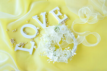 "LOVE"の文字と真珠とリボンとオーガンジーと白い花のリースのデザイン（黄色の背景）