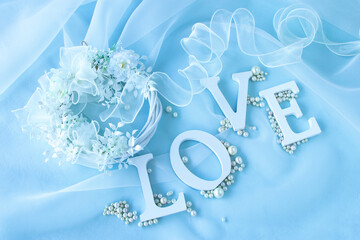 "LOVE"の文字と真珠とリボンとオーガンジーと白い花のリースのデザイン（水色の背景）