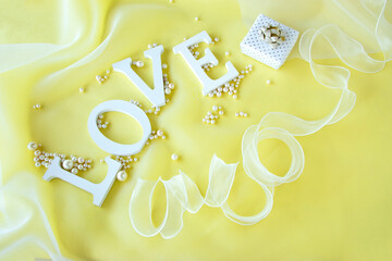 "LOVE"の文字と真珠とリボンとオーガンジーとプレゼントのデザイン（黄色の背景）