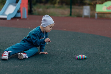 boy with down syndrome is sitting on a rubber covering on the playground, reaching for a toy