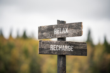 vintage and rustic wooden signpost with the weathered text quote relax recharge, outdoors in nature. blurred out forest fall colors in the background.