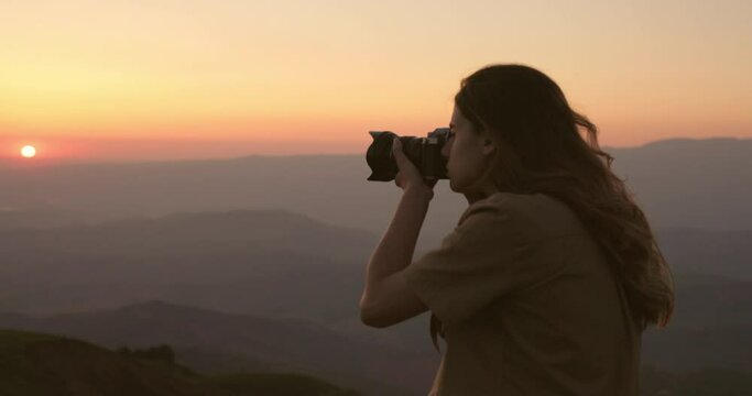 Close up shoot, a woman artist photographer takes stunning pictures of a sunrise in the mountains. A woman with a professional camera takes a photo in the mountains, standing on the edge of a hill.