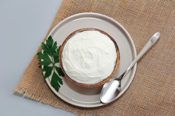 White fermented milk yogurt in a wooden decorative plate and a metal spoon on a brown background