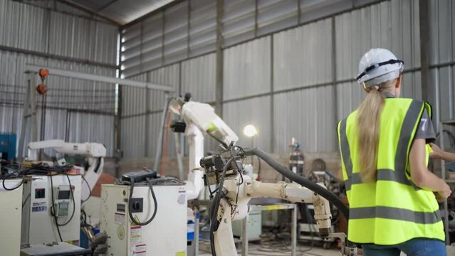In robotic training instructor teach girl engineer to program robot arm look manual from laptop
