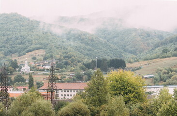Fototapeta premium Mountain from view with small village and flow fog. Foggy summer morning in the mountains and a small village. Country road in the mountains. Carpathians. Polyana. Ukraine
