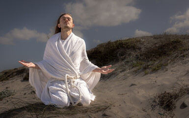 man in white robe in desert meditating and praising looking to heaven