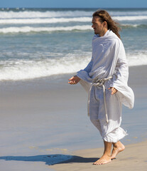 Man in Jesus-type white robes walking on beach with open arms