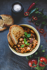 Vegan mixed bean bowl decorated with herbs, spices, vegetables and fresh roasted bread