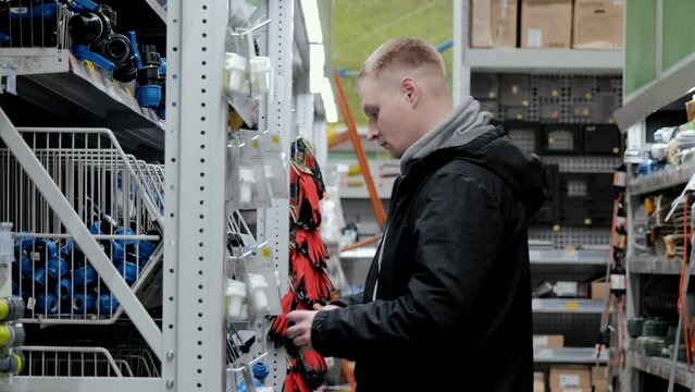 Large hardware store. Young man in a hardware store. A man in a hardware store chooses accessories for watering the lawn. Construction supermarket
