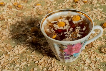 Dry chamomile flowers- tea time. Cup on yellow floral background